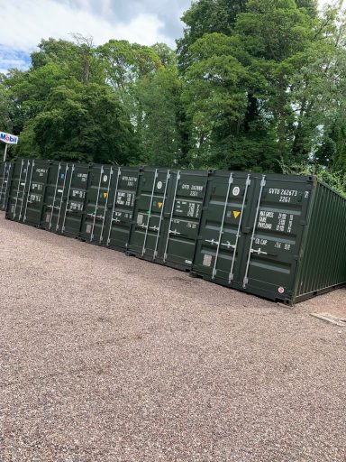 Rows of green shipping containers lined up near a tree-lined area.